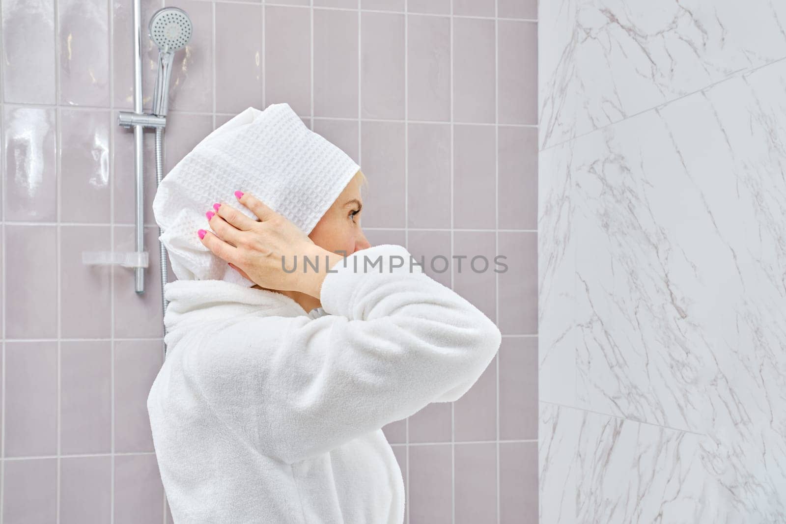 Middle aged woman in bathrobe wrapping her hair in towel after shower