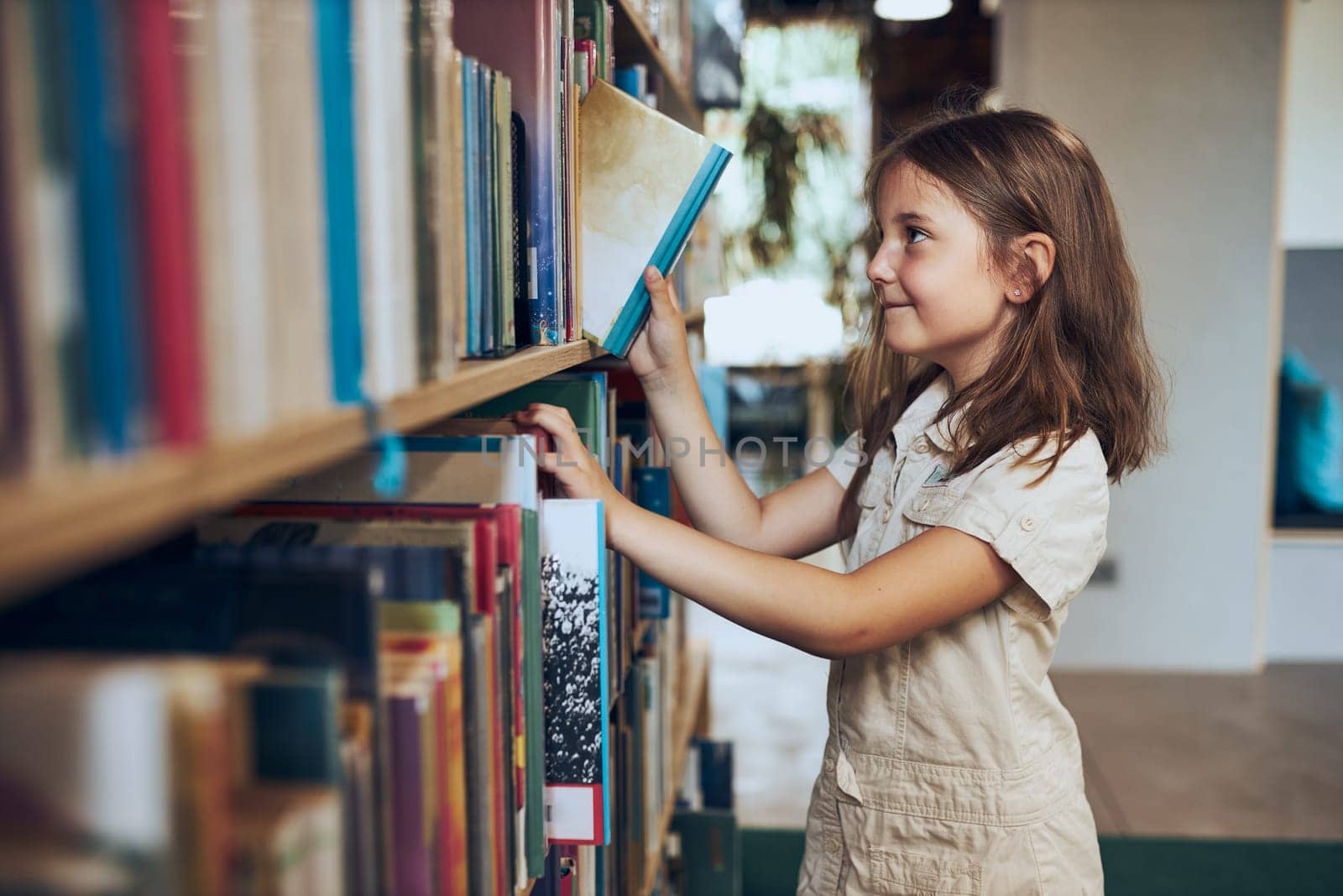 Schoolgirl choosing book in school library. Smart girl selecting literature for reading. Books on shelves in bookstore. Learning from books. School education. Benefits of everyday reading. Child curiosity. Back to school