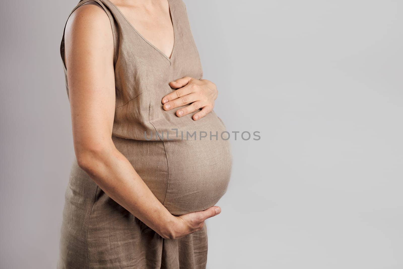 Pregnant woman touching her tummy standing over plain background. Pregnancy, expectation, motherhood concept