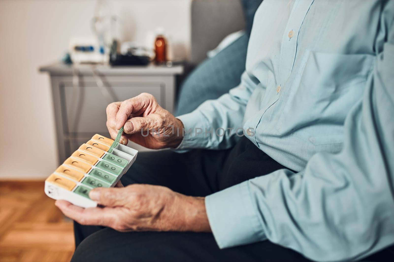Senior man patient opening pill dispenser to take next medicine dose. Organising medication