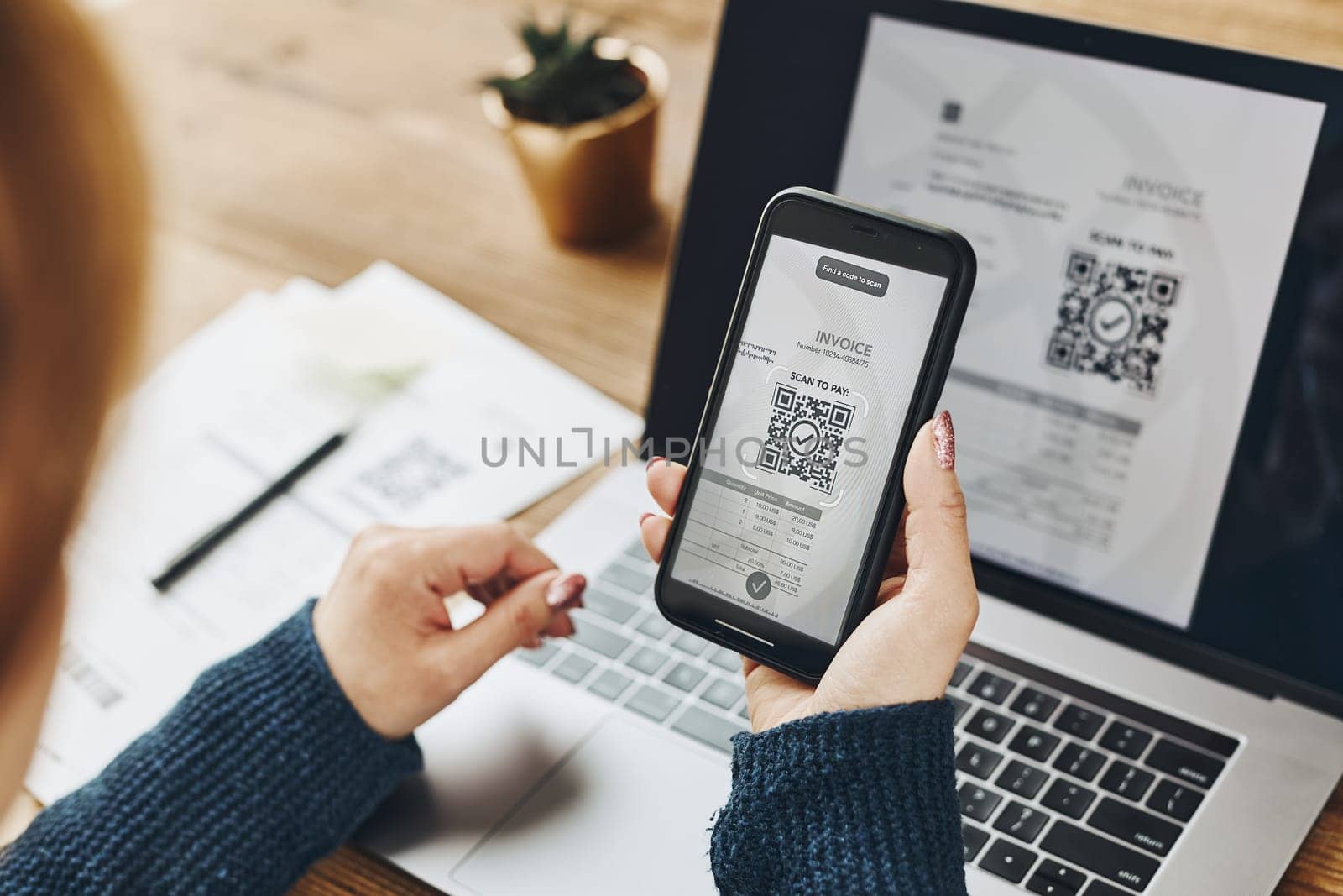 Woman scanning QR code from invoice to make payment using fast secure payment system and smartphone code reader. Business woman paying bills using express payment technology. Female using mobile phone and laptop. Paying expenses online. QR scanner. Making payment