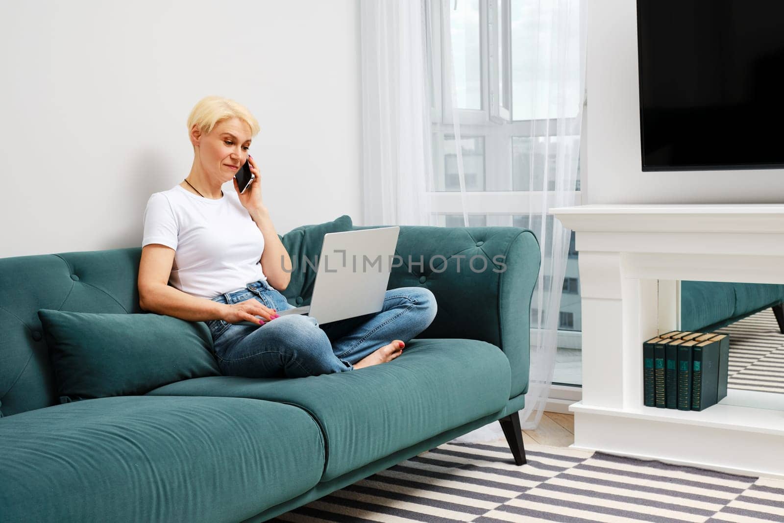 Middle-aged woman solves everyday problems remotely using laptop and smartphone