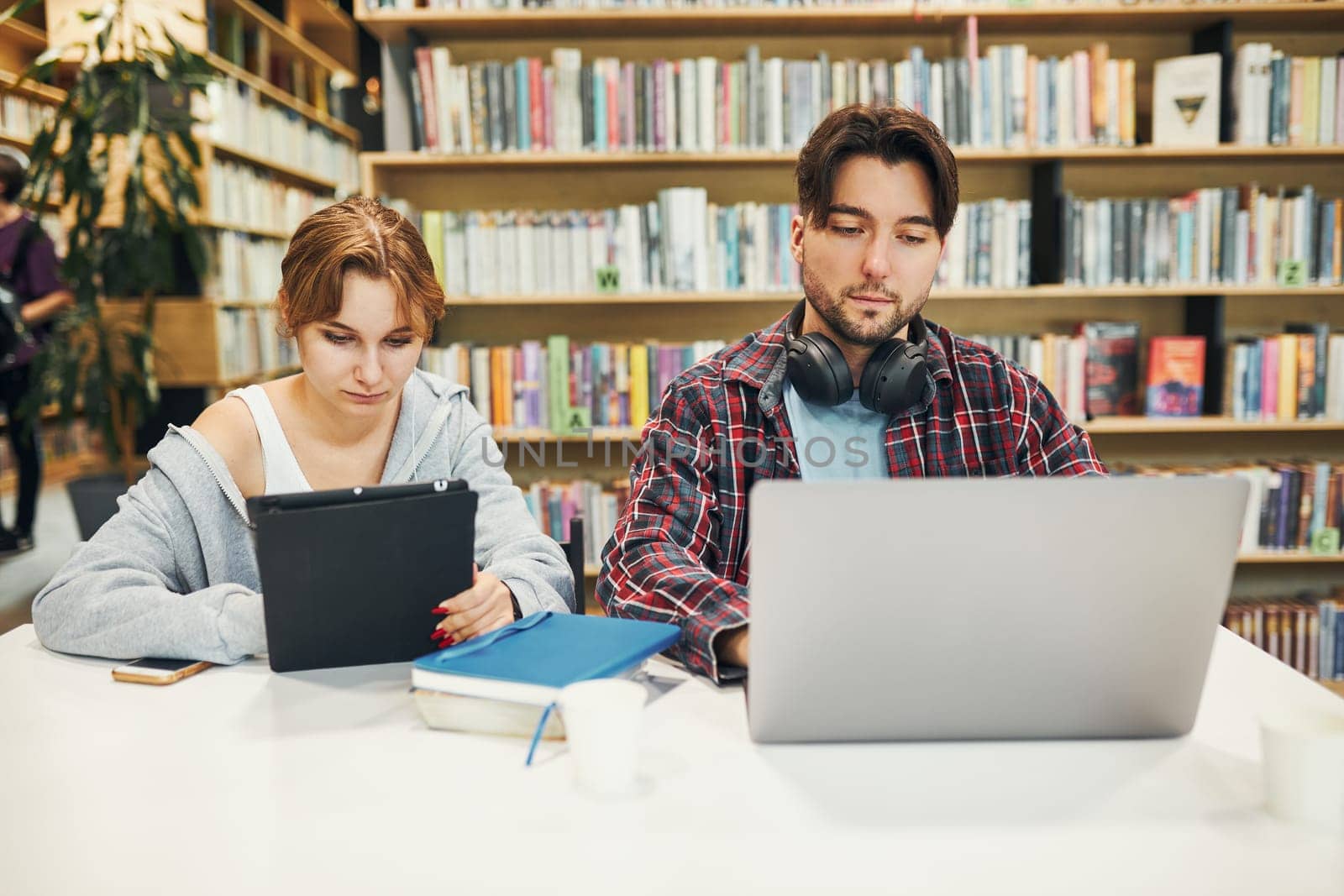 Students learning in university library. Young man preparing for test on laptop. Girl writing essay and making notes using computer. Focused students studying for college exams. Students discussing and learning together sitting at desk. Back to school