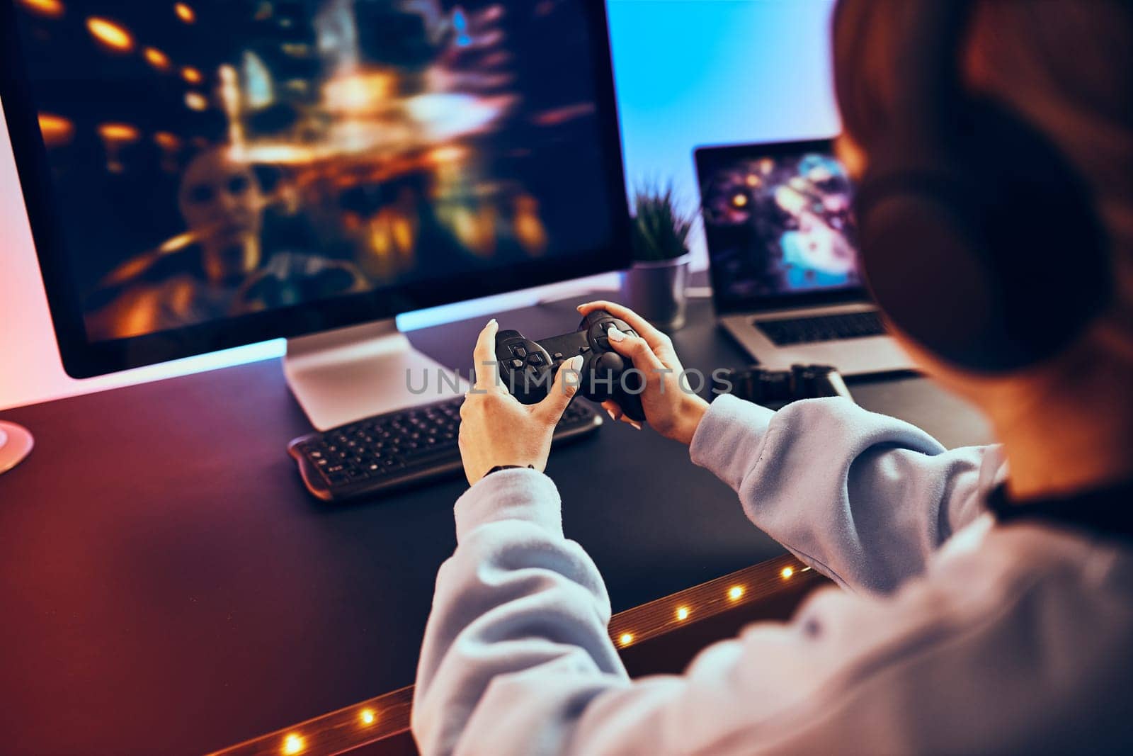 Teenager girl playing video game at home. Gamer holding gamepads sitting at front of screen. Streamer playing online in dark room lit by neon lights. Competition and having fun