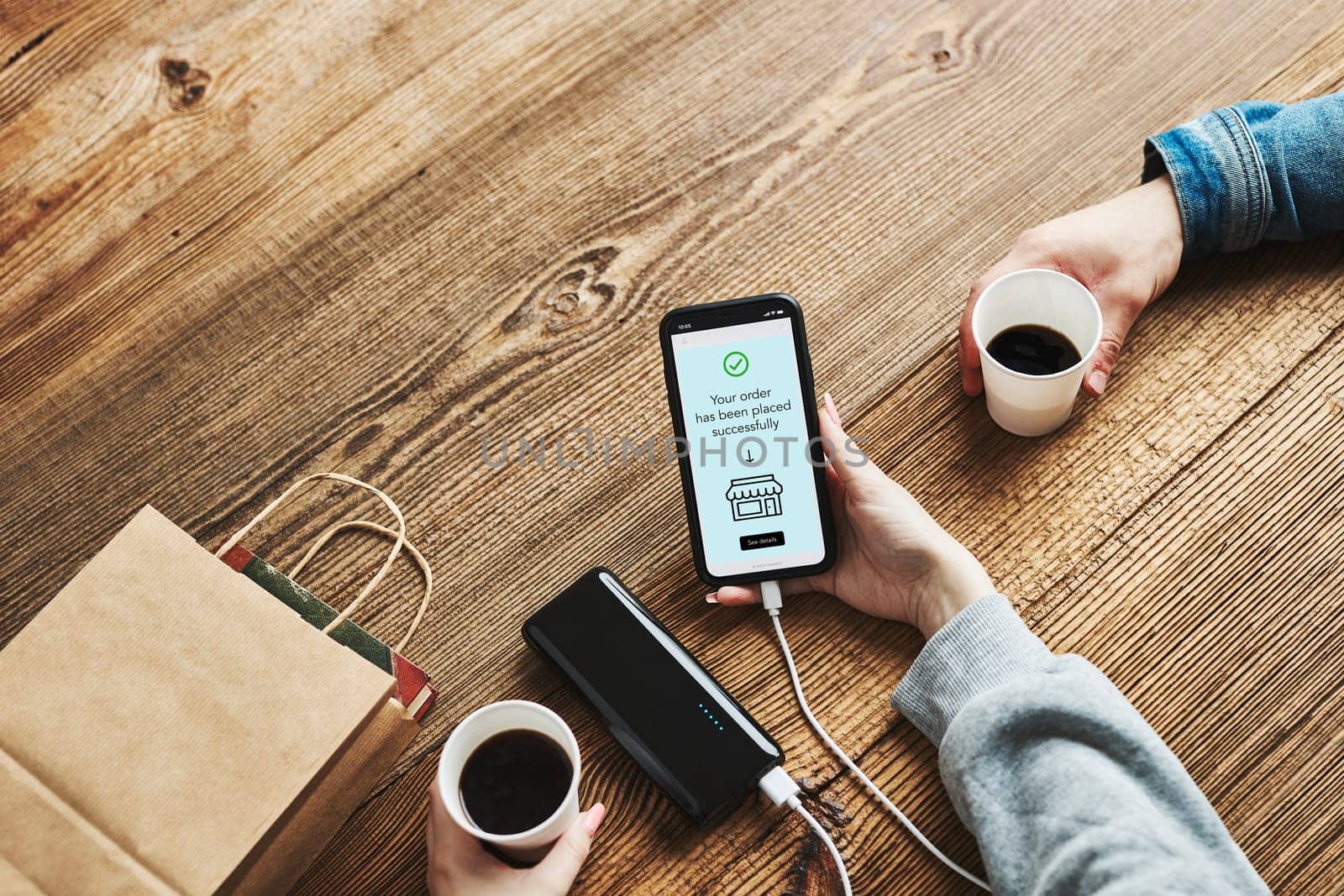 Online shopping. Paying online. Ordering product in online shop using smartphone. Payment confirmation on screen. Online banking. Paying for online shopping while charging mobile phone from powerbank in coffee shop