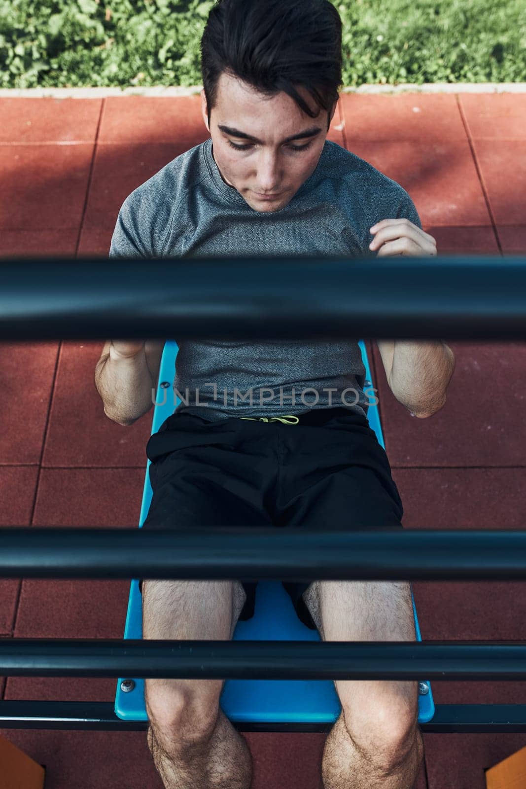 Young man doing sit-ups during his workout in a modern calisthenics street workout park. Man sitting on a sit-up board wearing sportswear