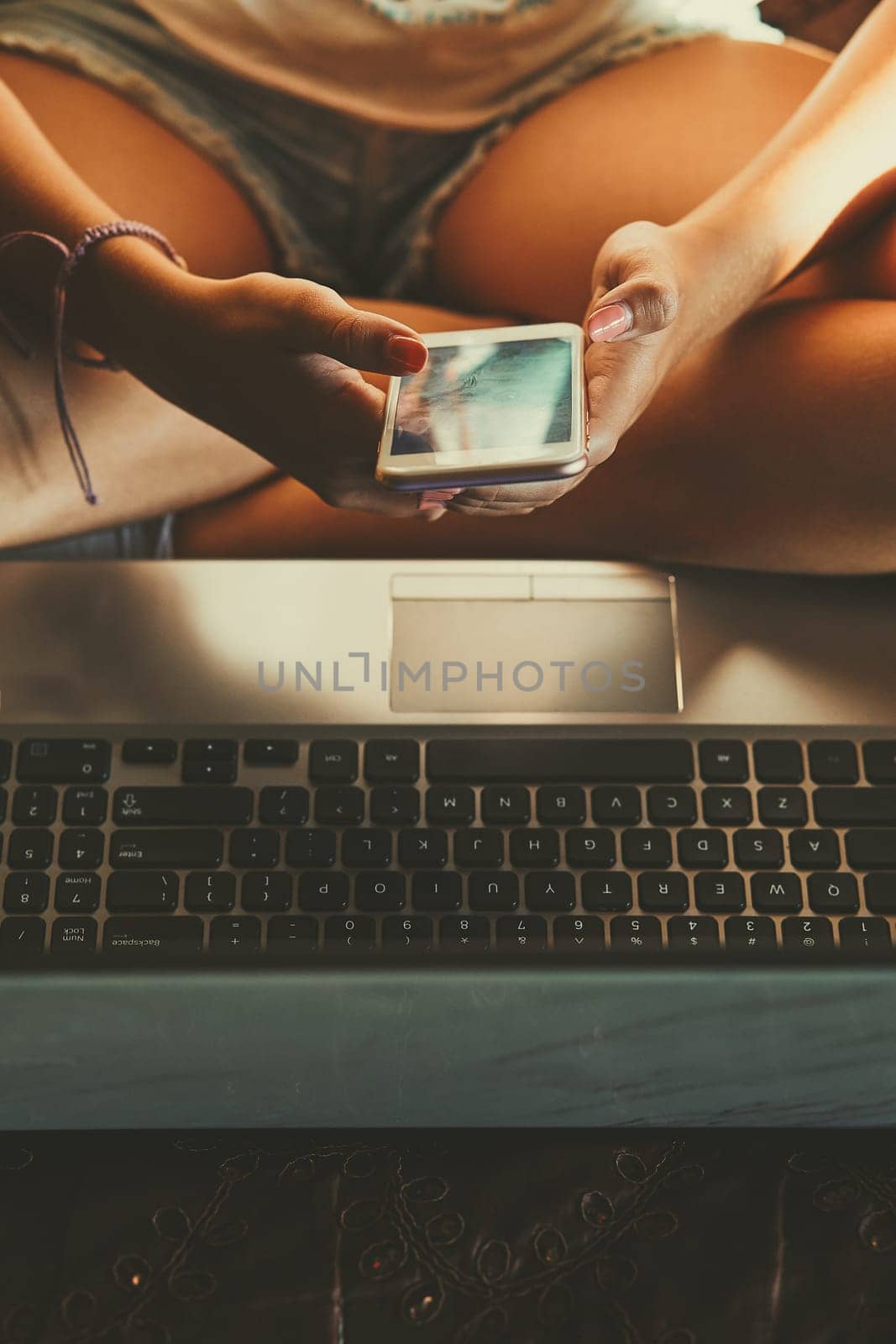 Young woman using portable computer and mobile phone, sitting on a bed, learning online at home. Candid people, real moments, authentic situations
