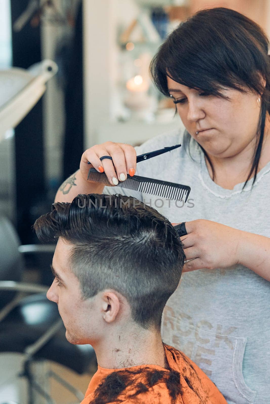 Hairdresser haircutting styling young man's hair in barbershop. Young woman working as a hairdresser in hair salon. Real people, authentic situations