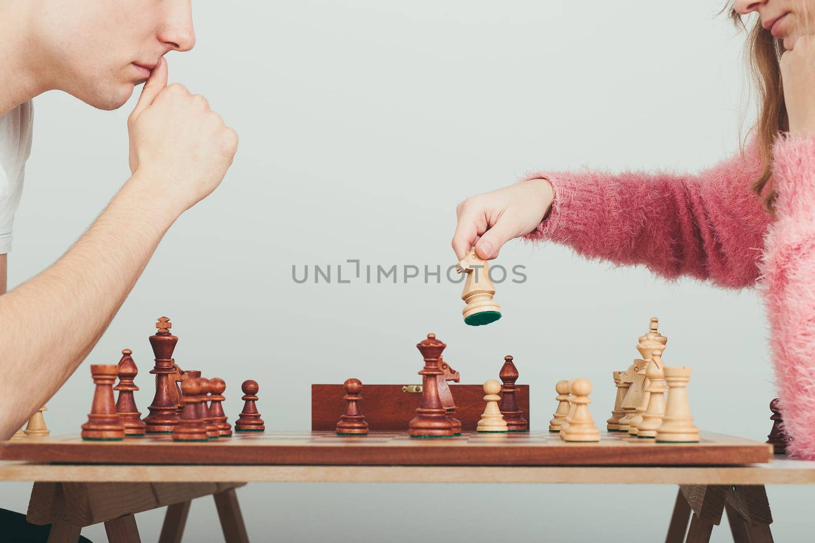 Girl and boy playing chess at home. Girl moving her piece. Teenagers sitting by a table. Profile view. Copy space for text at the top and bottom of image