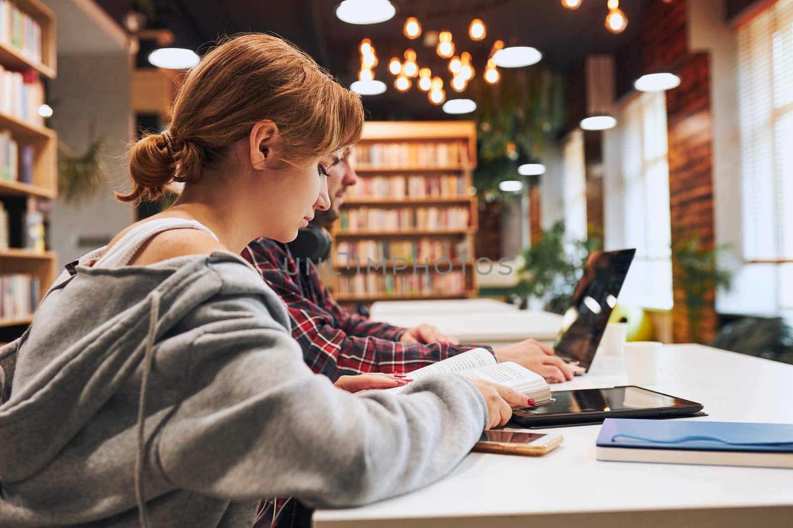 Students learning in university library. Young man preparing for test on laptop. Girl learning from book. Focused students studying for college exams. Students discussing and learning together sitting at desk. Back to school