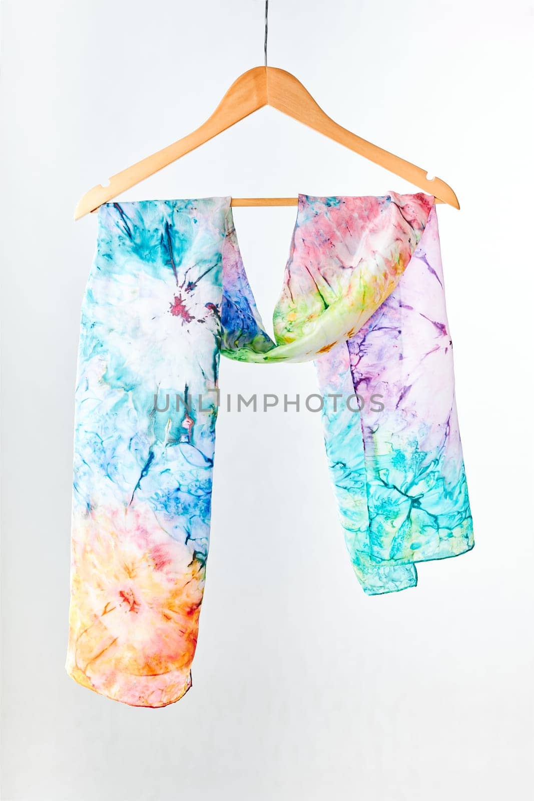 Silk colourful hand painted tied scarf hung on hanger over grey background. Woman fashion, tying a scarf, wearing a scarves. Stylish ways to tie and wear scarves