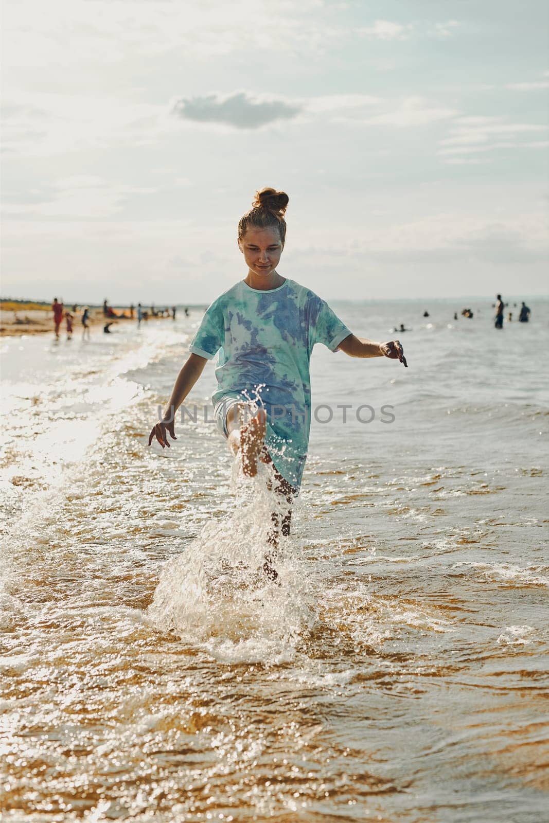 Girl splashing a water towards camera enjoying a free time over sea on a beach at sunset during summer vacation