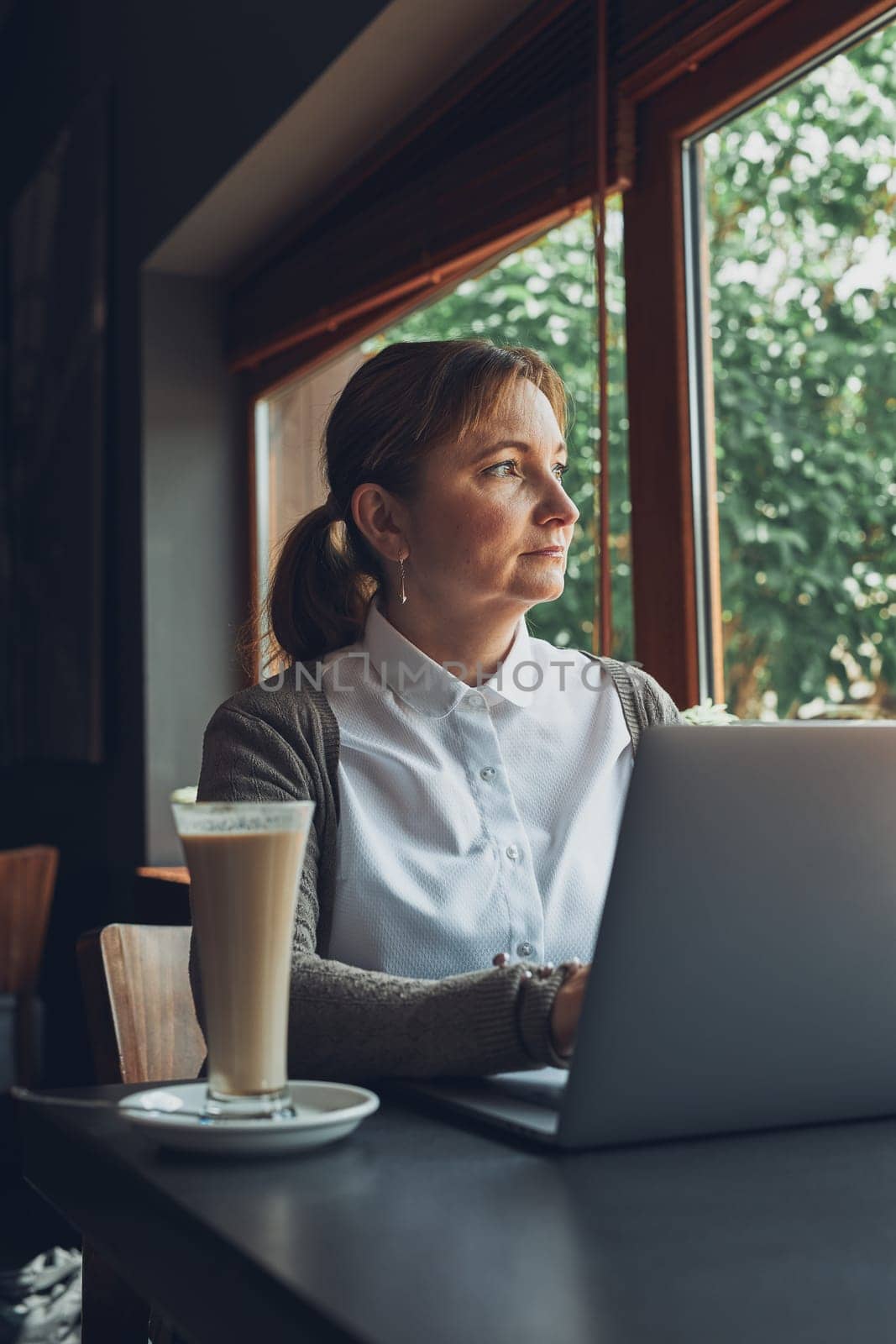 Relaxed businesswoman working remotely on her laptop computer contemplate managing her work sitting at the table in a cafe