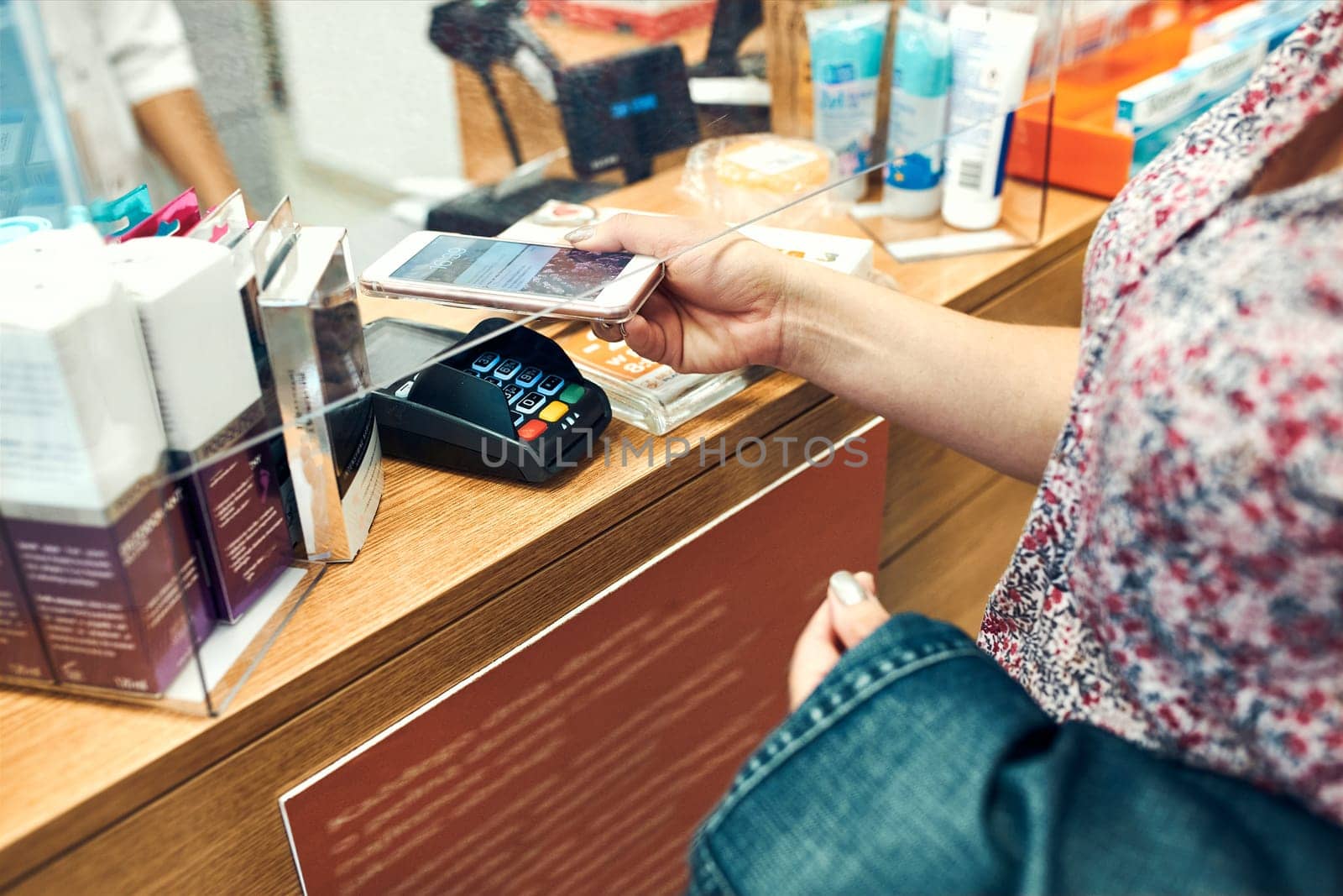 Woman paying for medicines at pharmacy using contactless method of payment via mobile phone. Woman using new way of payments