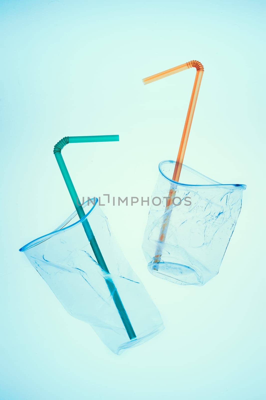 Squashed plastic cups and drink straws over blue background. Collecting plastic waste to recycling. Concept of plastic pollution and too many plastic waste. Copy space at the top