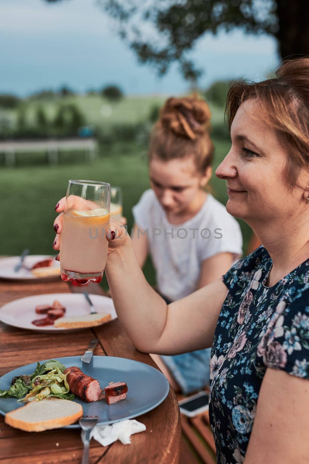 Family having a meal from grill during summer picnic outdoor dinner in a home garden. Close up of people sitting at a table with food and dishes
