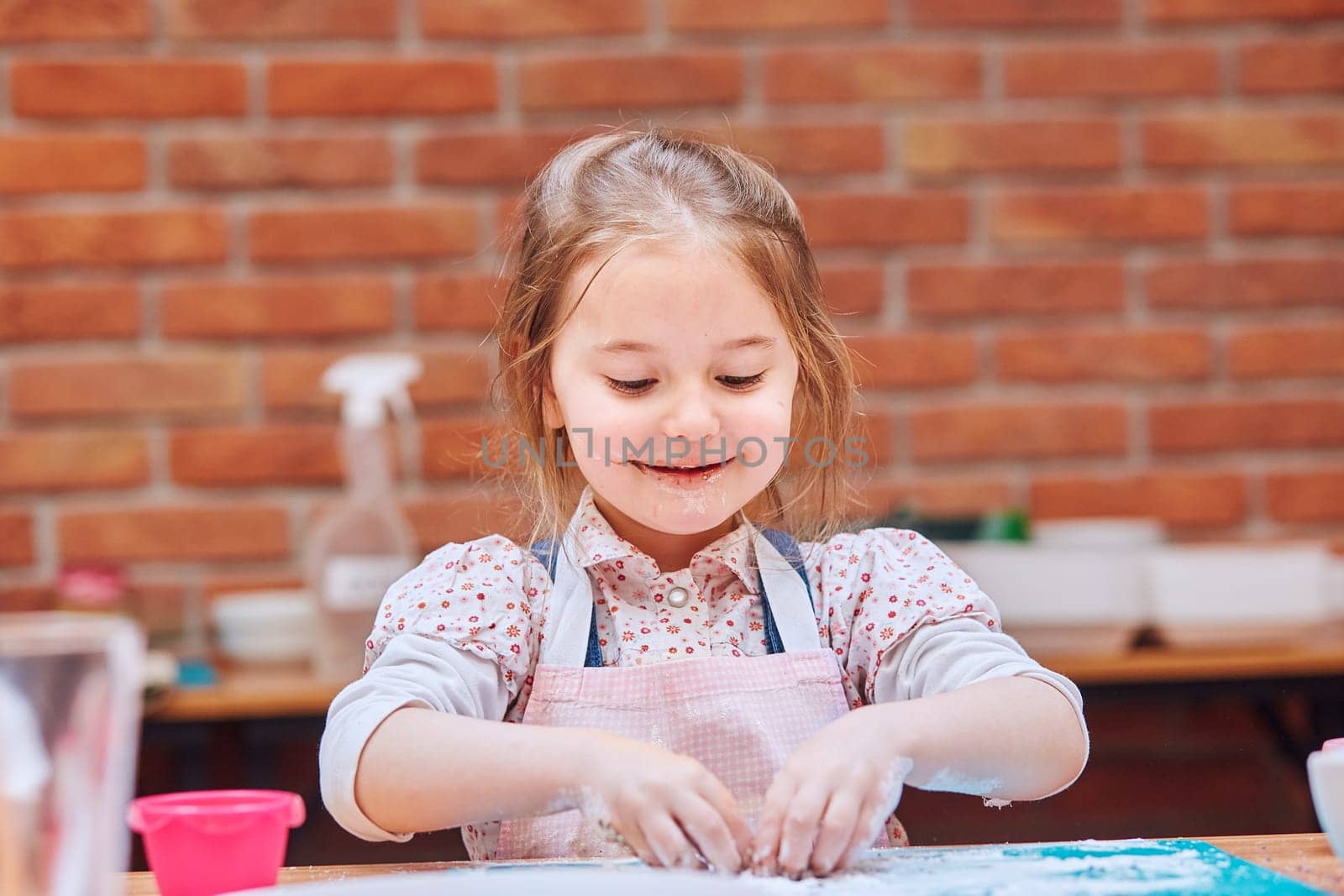 Little girl eating the icing sugar left after baking cookies. Kid taking part in baking workshop. Baking classes for children, aspiring little chefs. Learning to cook. Combining and stirring prepared ingredients. Real people, authentic situations