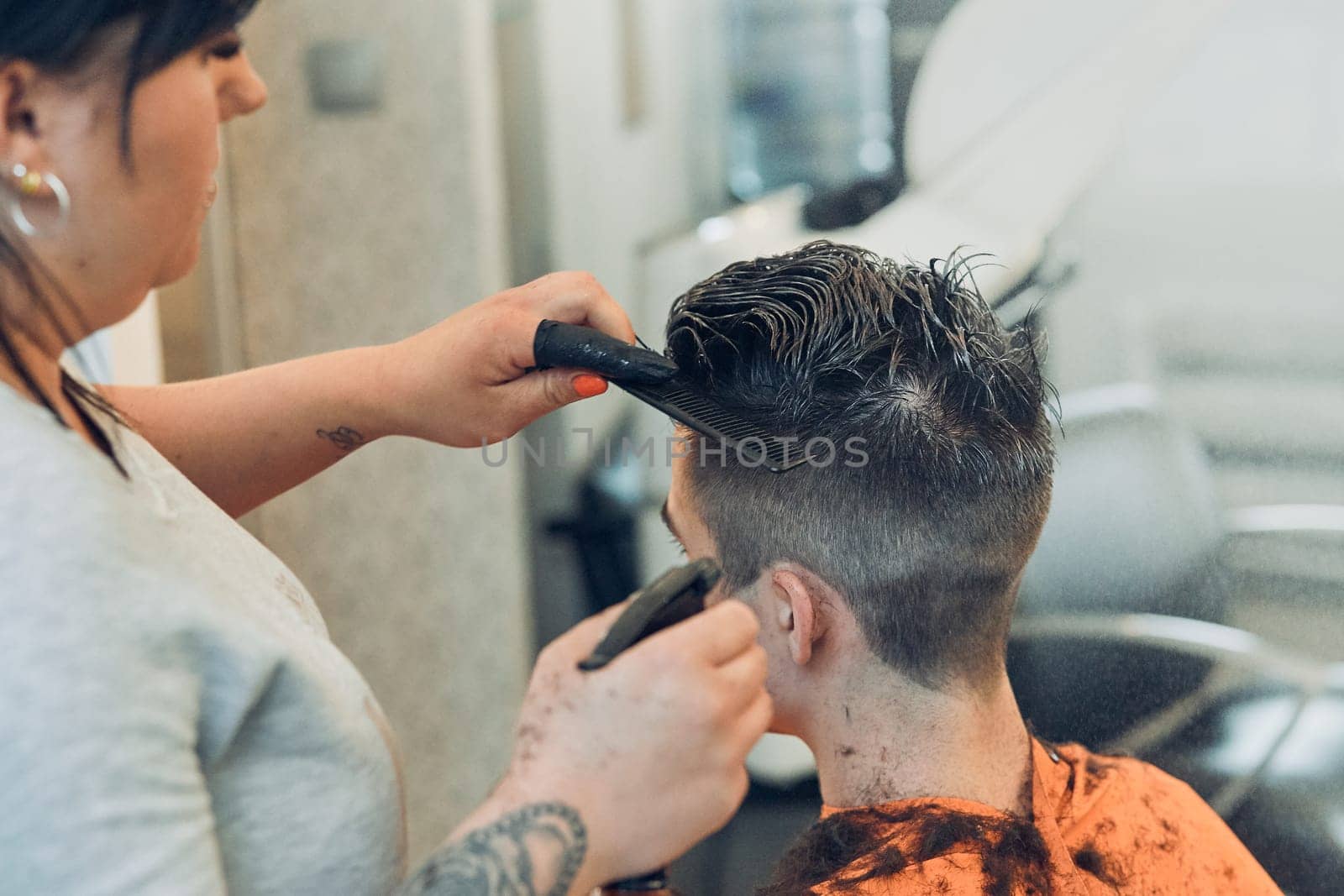 Hairdresser haircutting styling young man's hair in barbershop. Young woman working as a hairdresser in hair salon. Real people, authentic situations