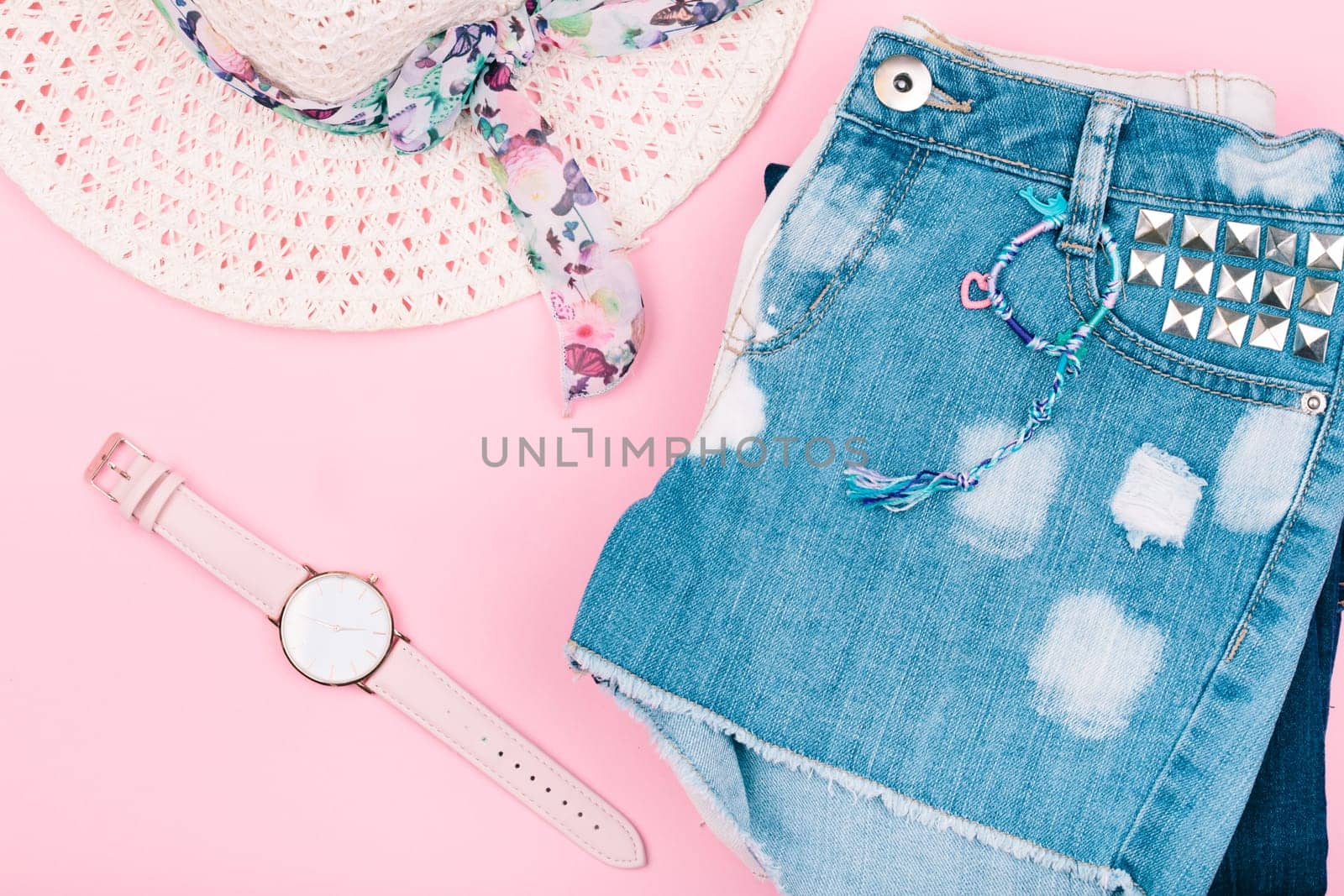 Female girlish clothes, blue jeans shorts, hat, watch on pink background
