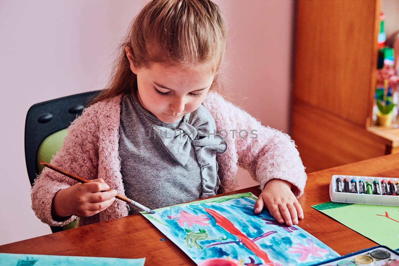 Little girl preschooler painting a picture using colorful paints and crayons. Child having fun making a picture during an art class in the classroom