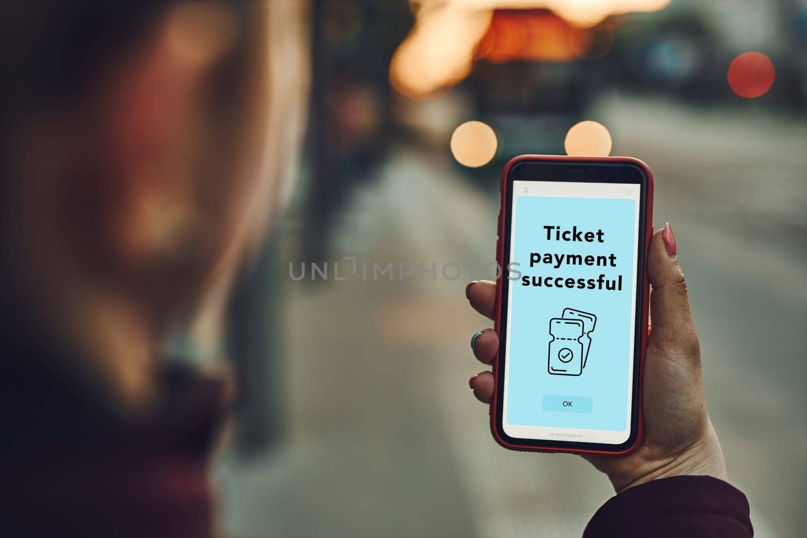 Woman buying ticket online at bus stop before ride. Person paying for ticket using mobile payment app. Using technology on the go. Order confirmation on mobile screen. Top up account in app. Bus lights in background