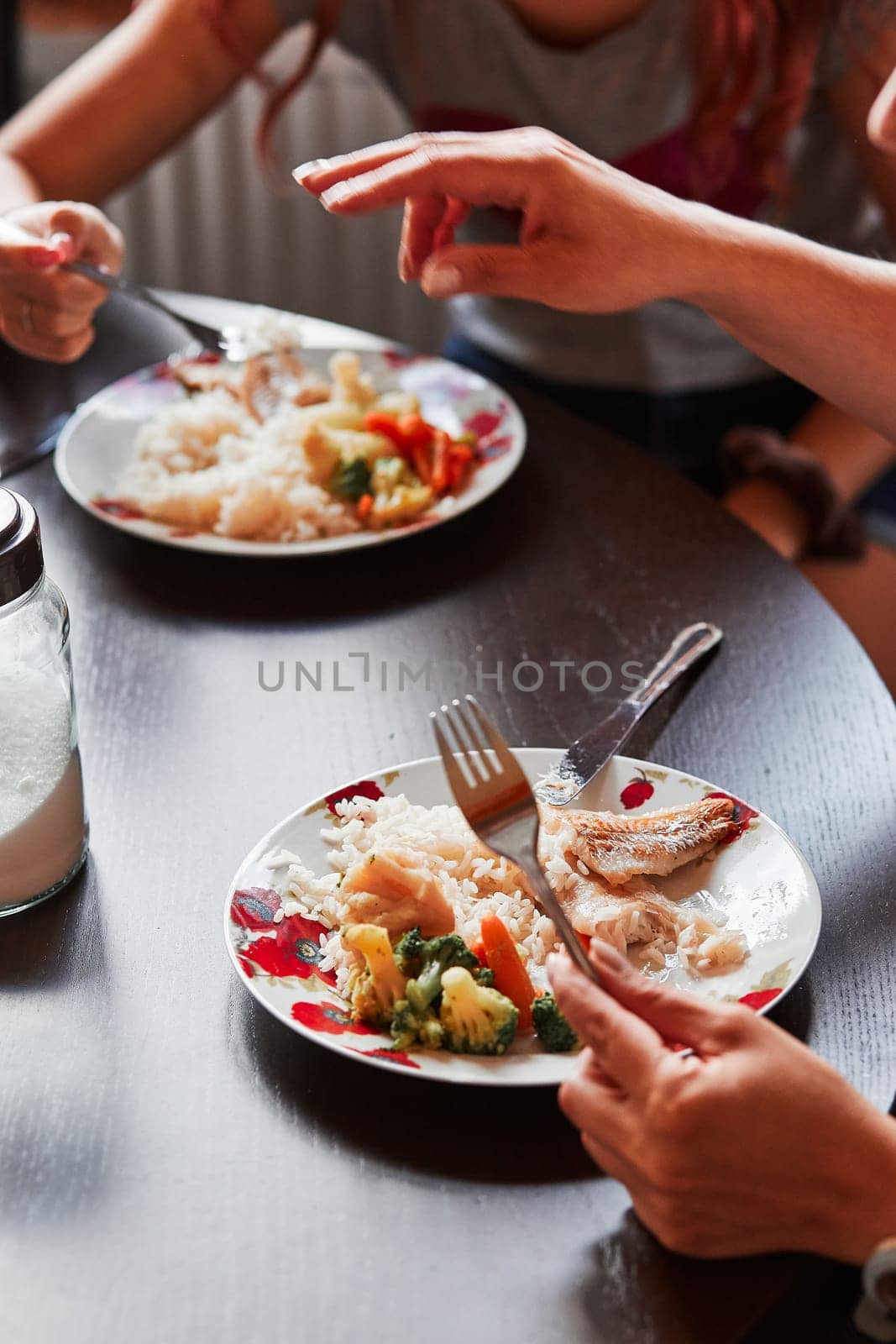 Closeup of the meal on plates on table and hands holding cutlery. People having a dinner at home. Real people, authentic situations