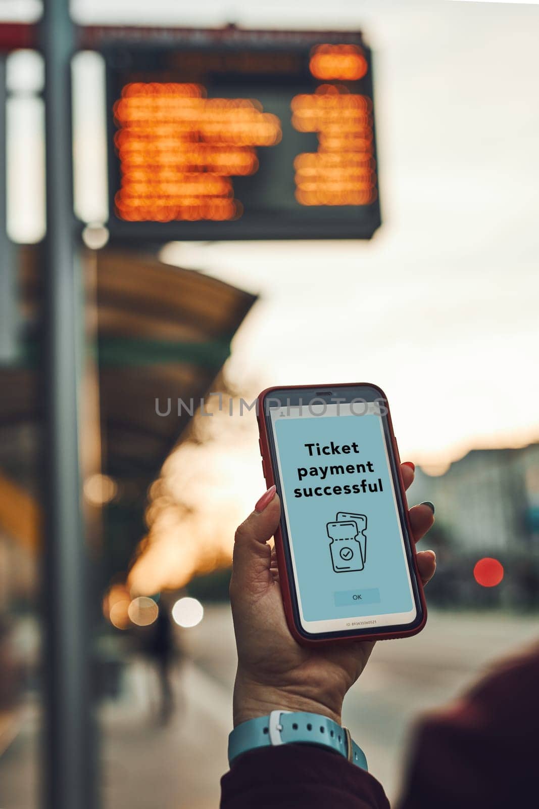 Woman buying ticket online near bus stop before ride. Person paying for ticket using mobile payment app. Using technology on the go. Order confirmation on mobile screen. Top up account in app. Bus routes schedule in background