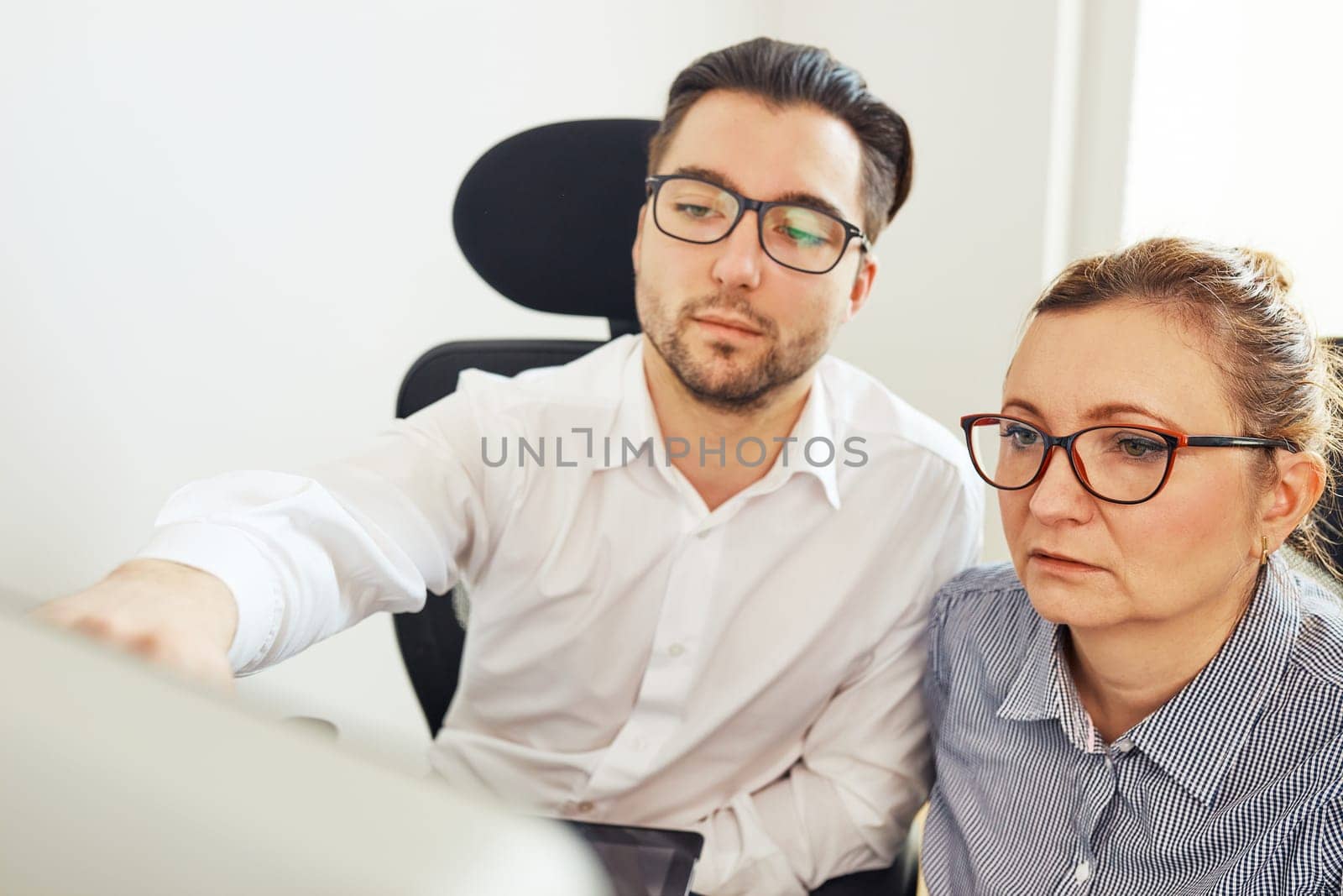 Two business people discussing financial data looking at computer screen. Entrepreneurs working hard sitting at computere screen in office. People having deadline working together. Workmates talking about project