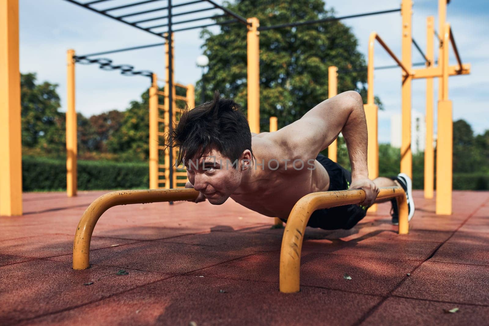 Young shirtless man bodybuilder doing push-ups on a parallel bars during his workout in a modern calisthenics street workout park