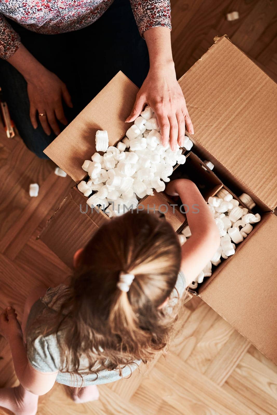 Woman unpacking a cardboard box parcel in room at home. Little girl waiting for opening a gift in package