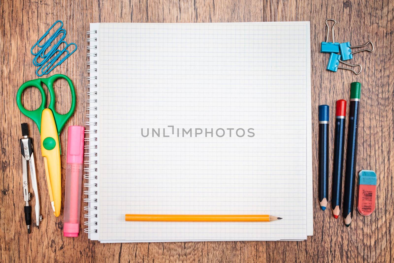 School accessories, pencil, pen, scissors, blank sheet of paper on a wooden desk. View from above