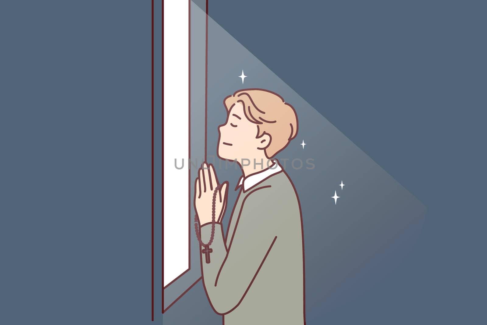 Religious man prays standing at window that emits light and holds chain with christian crucifix in hands. Believing guy prays turning to god is adherent of orthodox or catholic faith