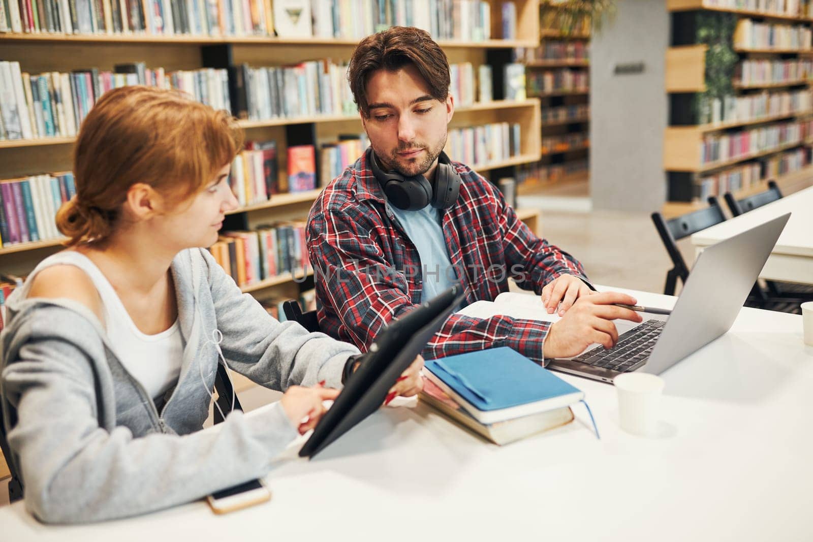 Students learning in university library. Young man preparing for test on laptop. Girl writing essay and making notes using computer. Focused students studying for college exams. Students discussing and learning together sitting at desk. Back to school