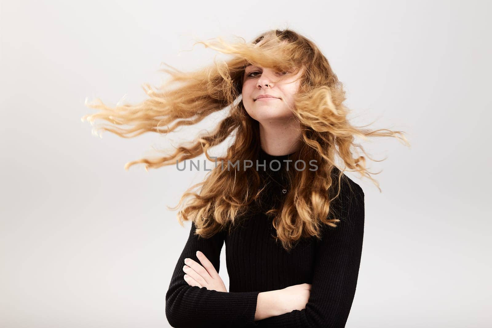 Portrait of pretty cheerful young woman waving tossing her hair holding arms crossed standing over a grey plain background