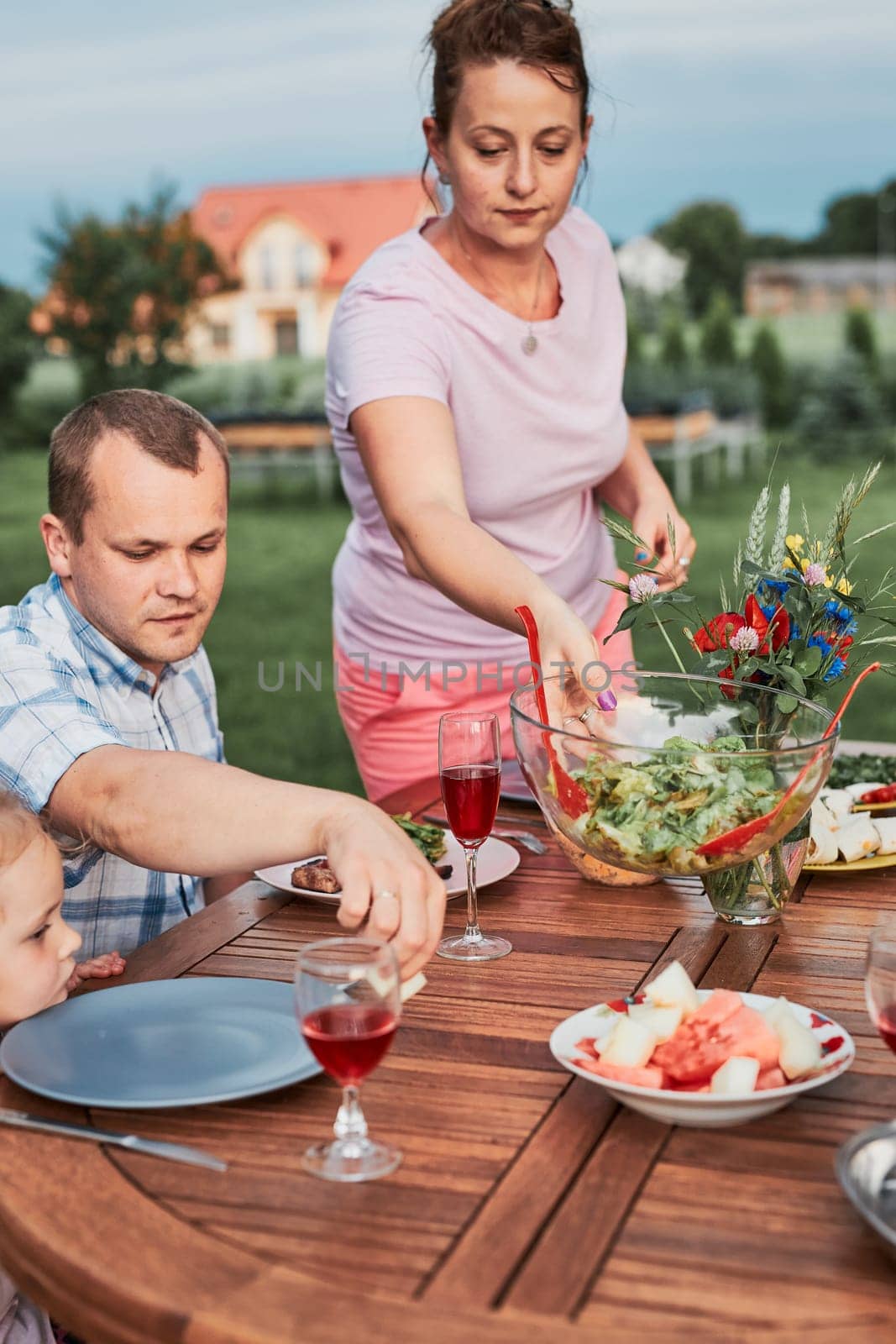Family having a meal from grill during summer picnic outdoor dinner in a home garden. Close up of people sitting at a table with food and dishes