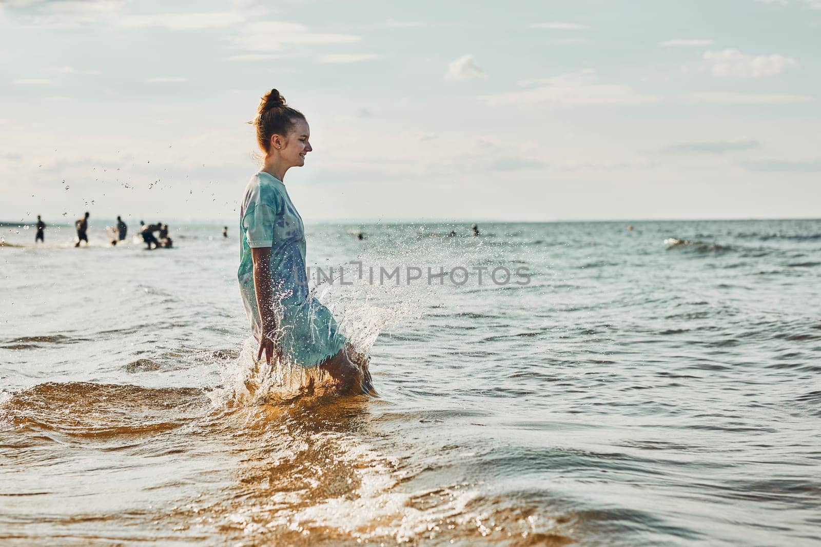 Girl enjoying sea jumping over waves spending a free time over sea on a beach at sunset during summer vacation