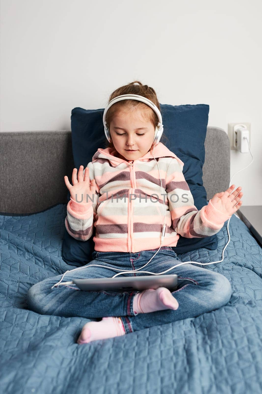 Little girl preschooler learning online solving puzzles playing educational games listetning to music and sounds using tablet and headpphones at home during pandemic quarantine