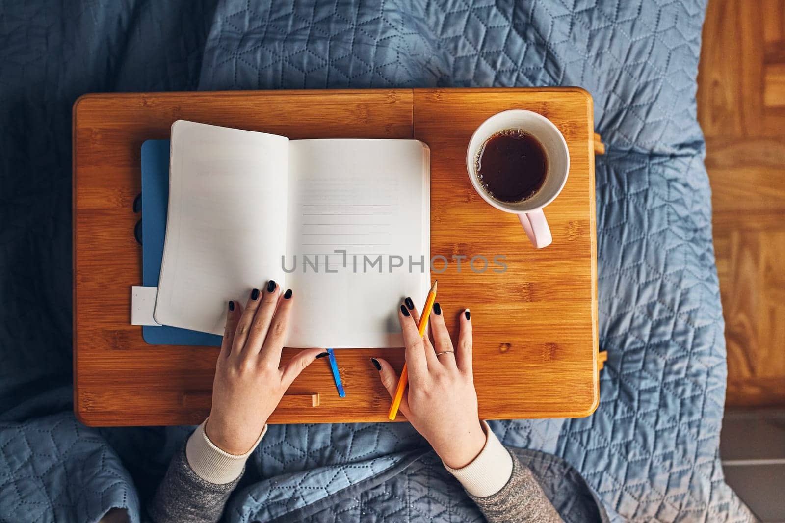 Student learning at home. Young woman making notes, reading and learning from notepad. Girl writing journal sitting in bed at home during quarantine