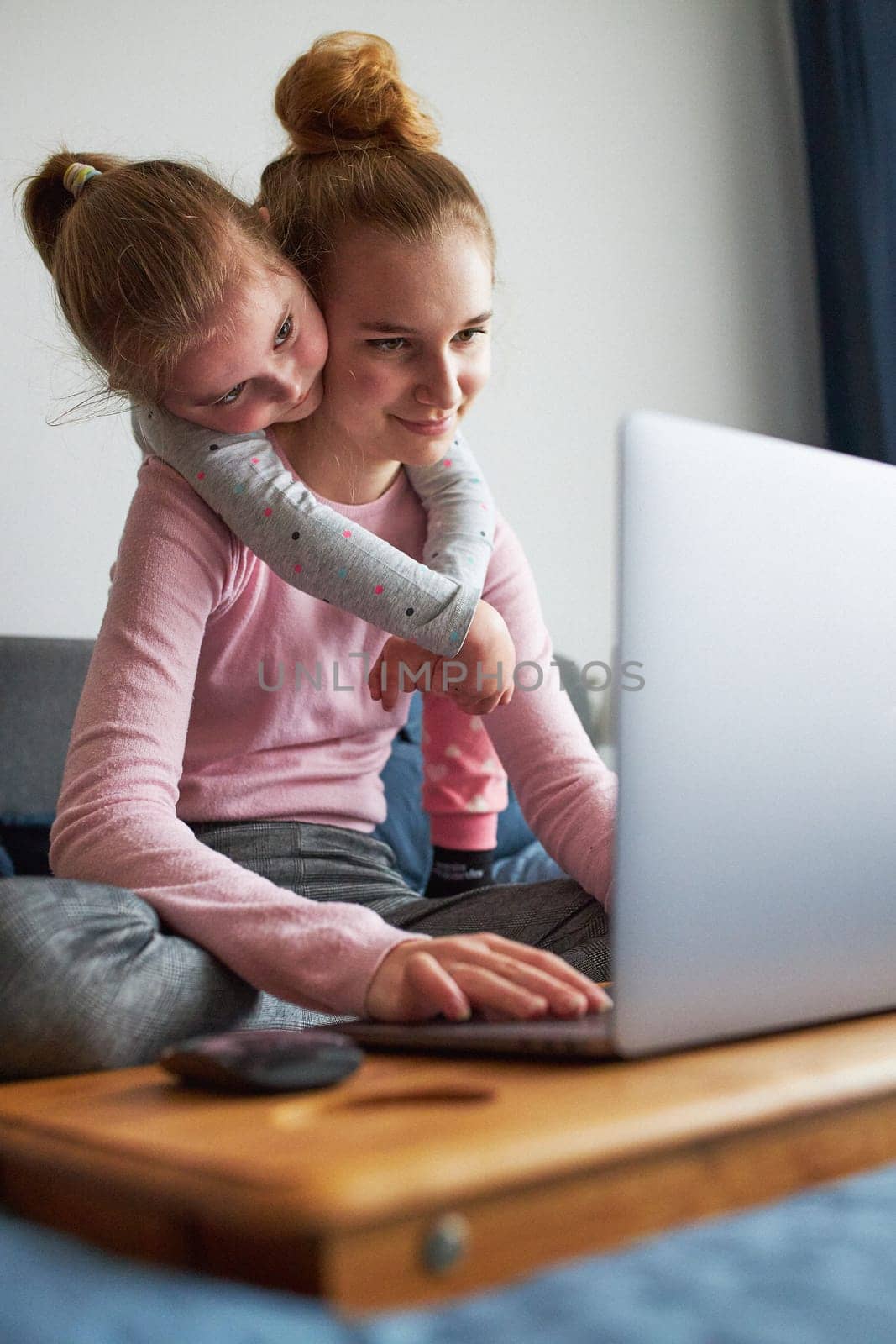 Grandchildren teenage girl and her younger sister talking on video call with granparents on laptop from home during COVID-19 quarantine. Girls sitting on bed in front of computer
