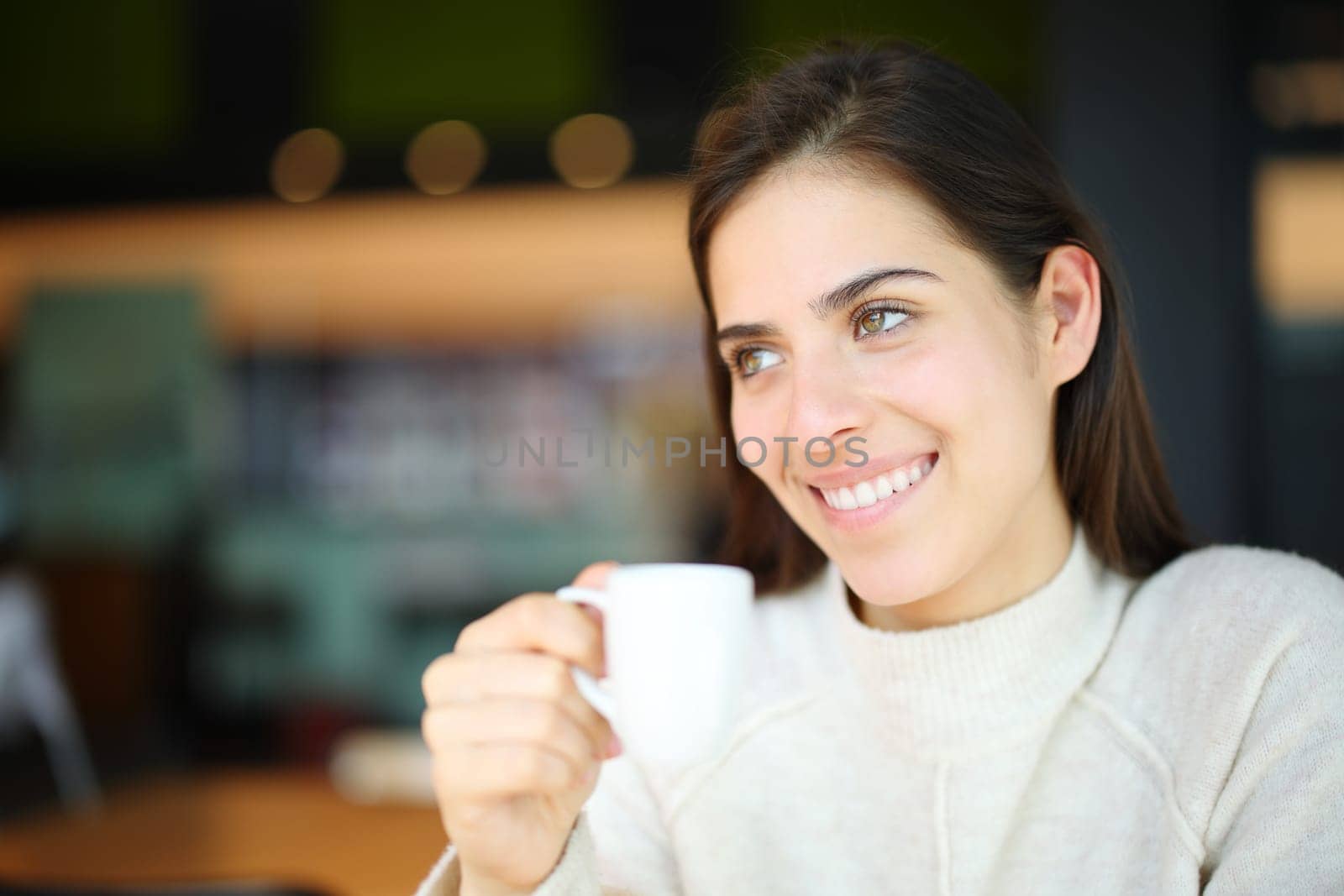 Happy woman smiling looks away holding cup in a coffee shop