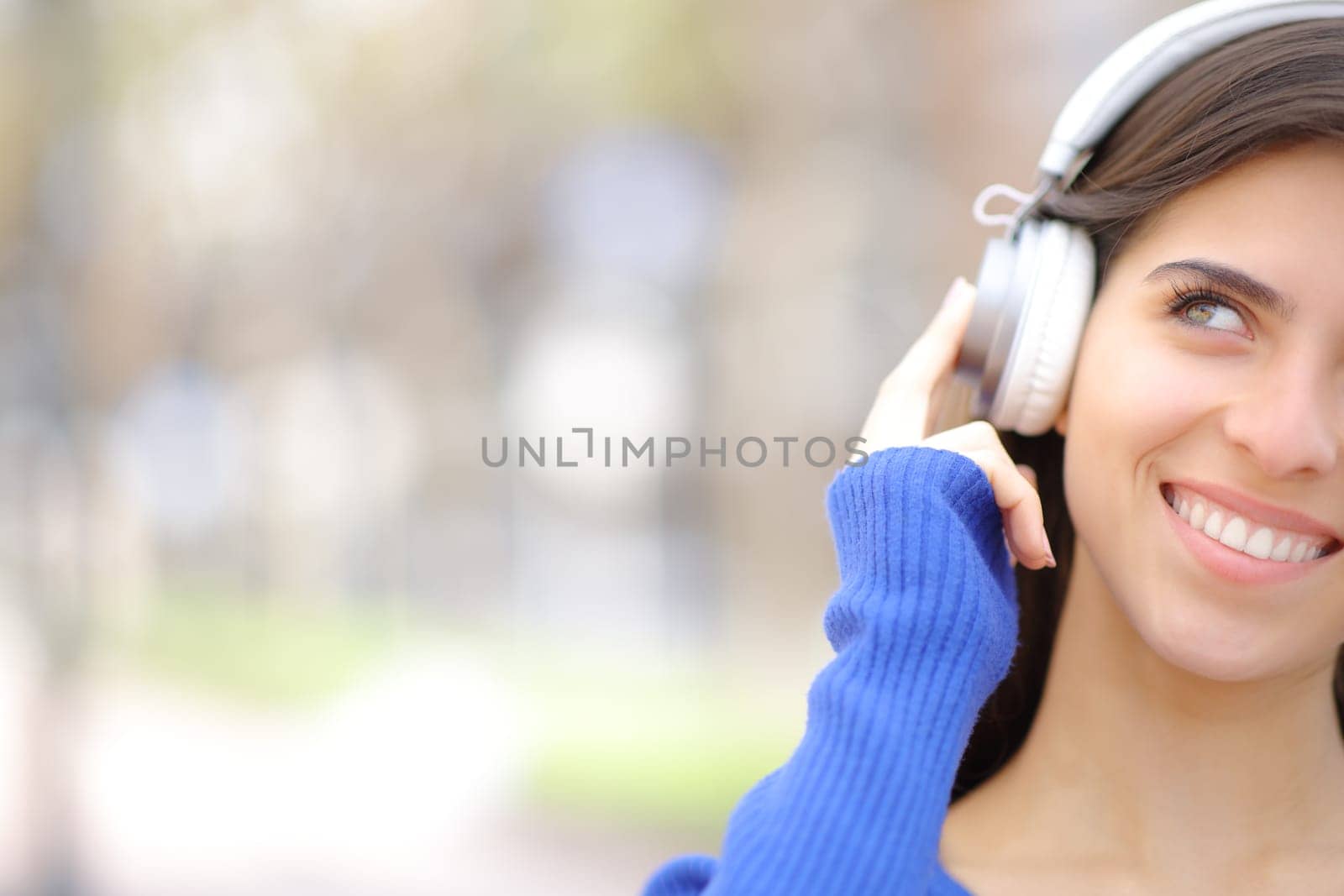 Front view portrait of a happy woman with headphone looks at side with copy space