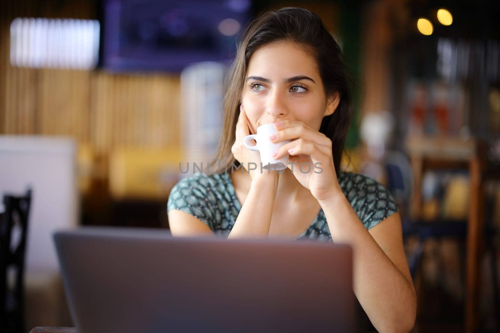 Distracted woman using laptop drinking in a coffee shop looking at side