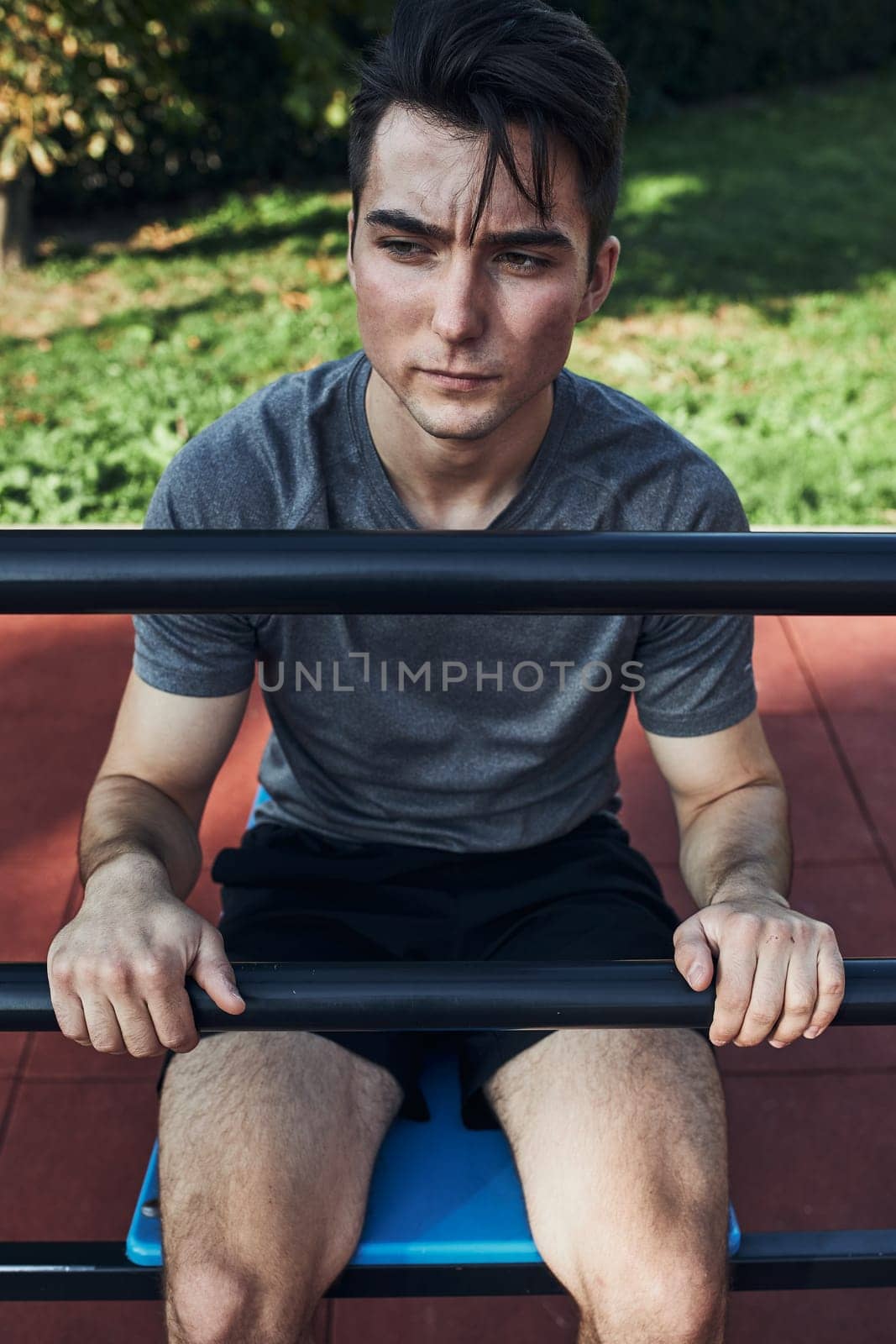 Portrait of young man having break during his workout in a modern calisthenics street workout park. Man sitting on a sit-up board wearing sportswear looking away