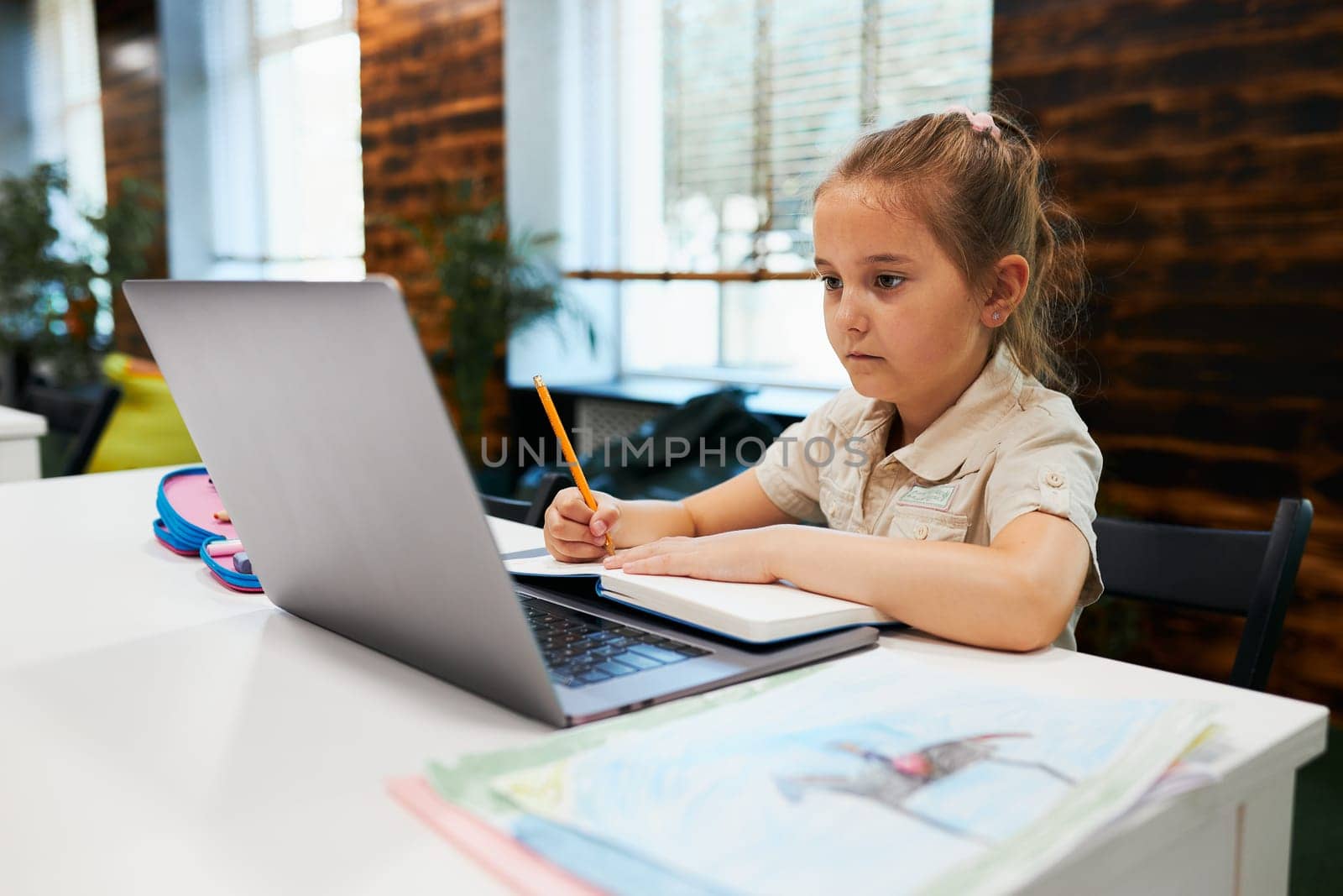 Engaged absorbed student doing her homework using laptop in after school club at primary school. Back to school. Child using technology on elementary computer science class. Smart little girl learning from educational application at school. Child solving riddles and puzzles on personal computer
