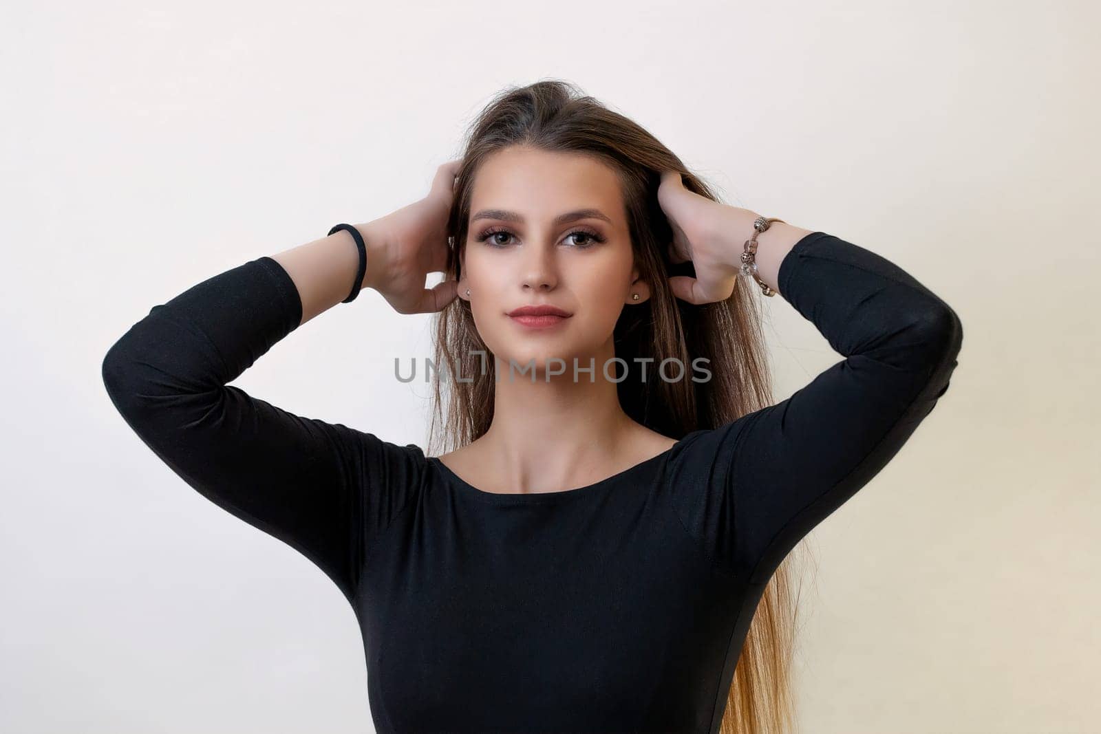 Front view of attractive brunette girl posing with hands in her hand on the light background. Horizontally.
