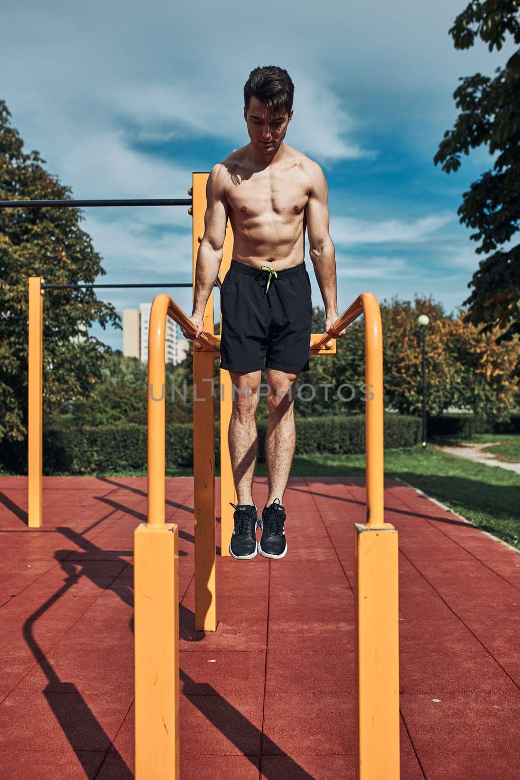 Young shirtless bodybuilder doing dips on parallel bars during his workout in a modern calisthenics street workout park