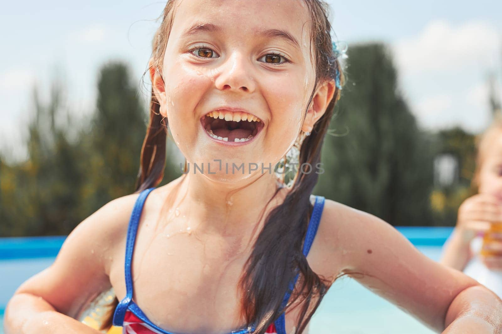 Portrait of happy smiling girl standing in a pool having fun on a summer sunny day. Close up of smiling kid looking at camera