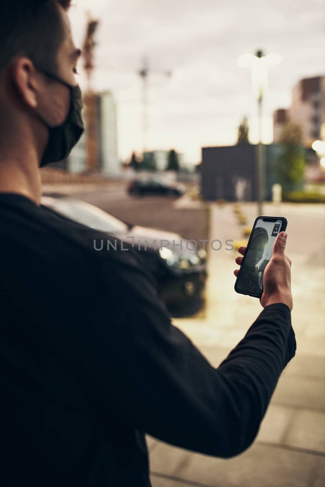 Young man talking on video call standing outdoors in the street in the evening wearing the face mask to avoid virus infection and to prevent the spread of disease in time of coronavirus