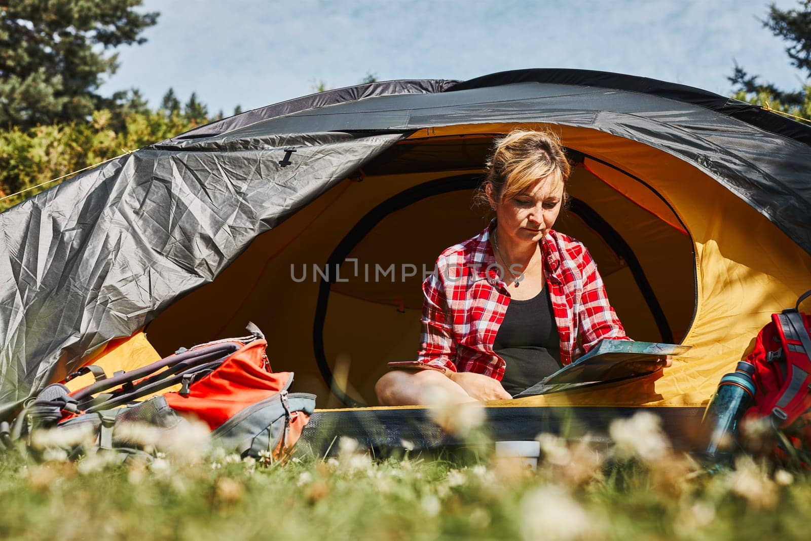 Woman planning next trip while sitting with map in tent. Woman relaxing in tent at camping during summer vacation. Actively spending vacations outdoors close to nature. Concept of camp life