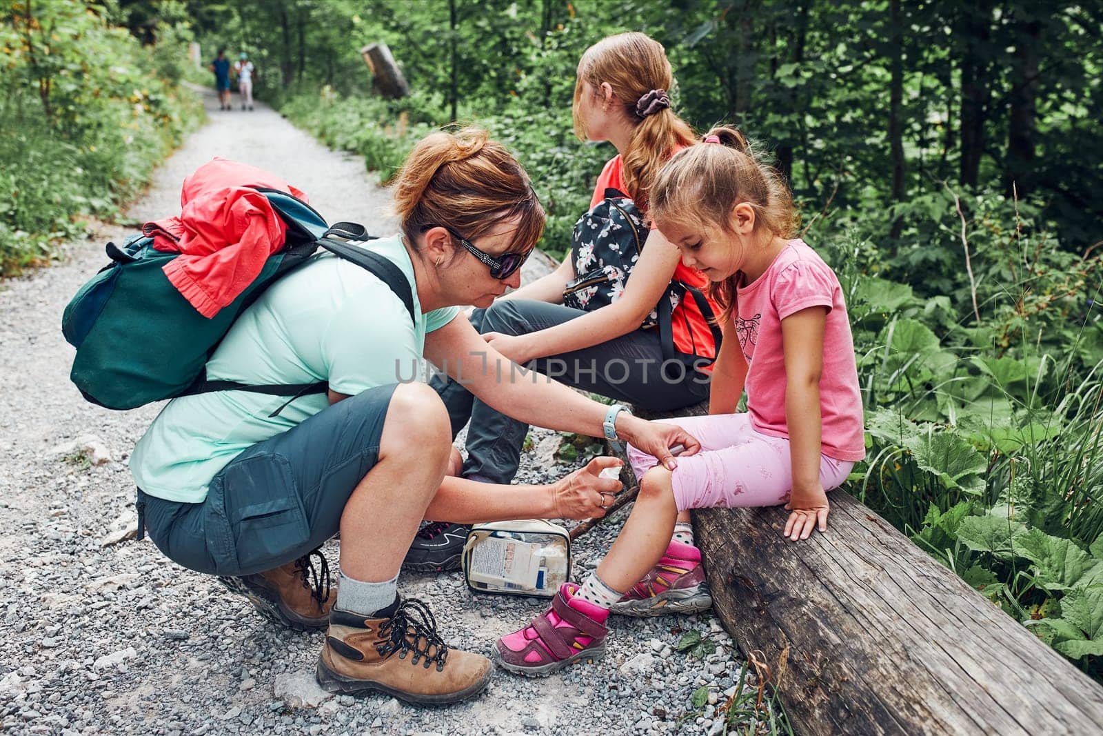 Mother dressing the wound on her little daughter's knee with medicine in spray. Accident happened during family summer vacation trip. People actively spending time